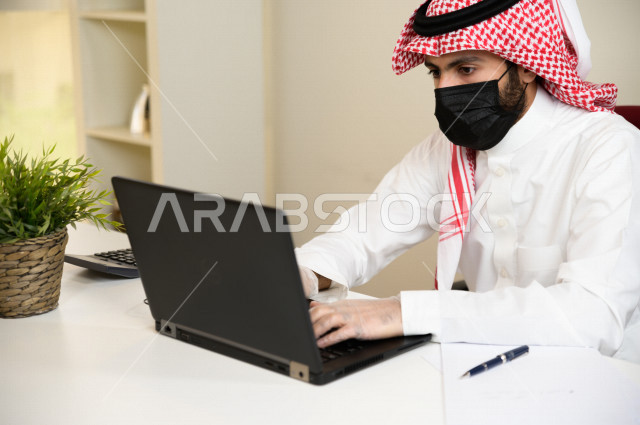 رجل اعمال عربي سعودي خليجي يرتدي الكمامة والقفازات لضبط انتشار العدوى ، استخدام الحاسوب المحمول لانجاز العمل ، القيام بالعمليات المحاسبية ، العمل عن بعد ، اجتماعات اونلاين ، التسويق الالكتروني