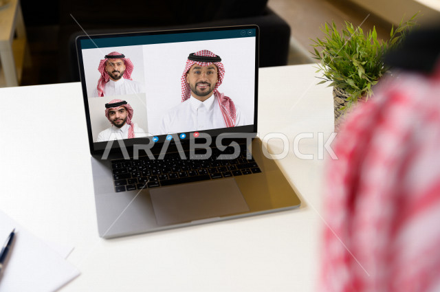 رجل اعمال عربي سعودي خليجي يجلس امام الحاسوب المحمول لانجاز الاعمال ، العمل عن بعد لمنع انتشار فايروس كورونا ، اجتماعات اونلاين ، التسويق الالكتروني ، التعليم الالكتروني