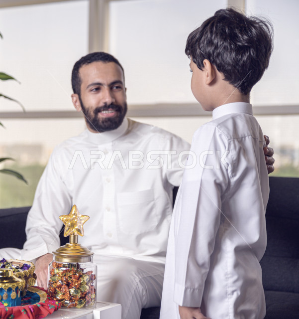 A wonderful participation of a Saudi Arabian Gulf father with his son on the morning of Eid, wearing the traditional Saudi dress, Eidiya, Gergean, Eid celebrations and manifestations, an official holiday, spending happy family times on Eid