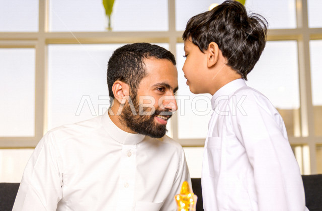 A Saudi Arabian Gulf child kissing his father's head on the morning of Eid with gestures indicating happiness and joy, wearing traditional Saudi dress, Eidiya, Gergean, celebrations and manifestations of Eid, spending happy family times on Eid