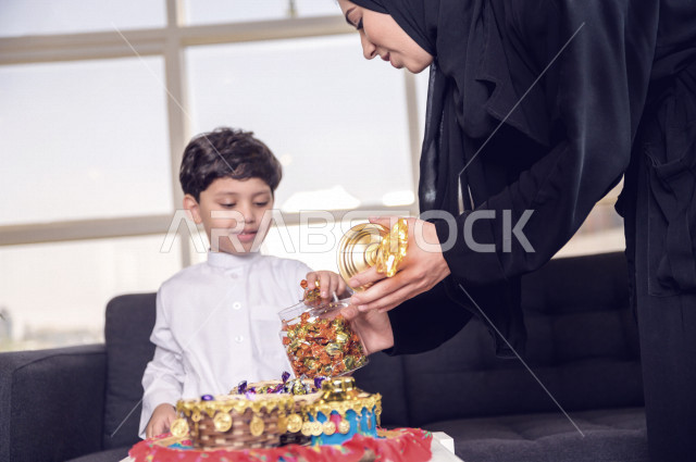 مشاركة رائعة لأم عربية خليجية سعودية مع ابنها في صباح يوم العيد تقوم بتقديم الحلوى له بإيماءات تدل على السعادة و الفرح ، ارتداء اللباس السعودي التقليدي ، العيدية ، القرقيعان ، احتفالات و مظاهر العيد ، قضاء أوقات عائلية سعيدة في العيد