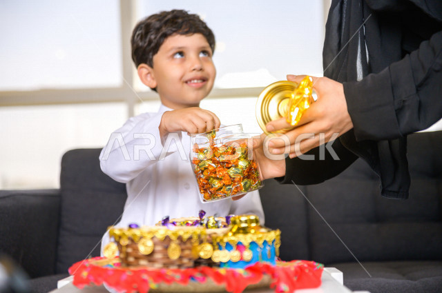 مشاركة رائعة لأم عربية خليجية سعودية مع ابنها في صباح يوم العيد تقوم بتقديم الحلوى له بإيماءات تدل على السعادة و الفرح ، ارتداء اللباس السعودي التقليدي ، العيدية ، القرقيعان ، احتفالات و مظاهر العيد ، قضاء أوقات عائلية سعيدة في العيد