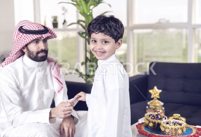 مشاركة رائعة لأب عربي خليجي سعودي مع ابنه في صباح يوم العيد ، تقديم العيدية بسعادة ، ارتداء اللباس السعودي التقليدي ، العيدية ، القرقيعان ، احتفالات و مظاهر العيد ، عطلة رسمية ، قضاء أوقات عائلية سعيدة في العيد