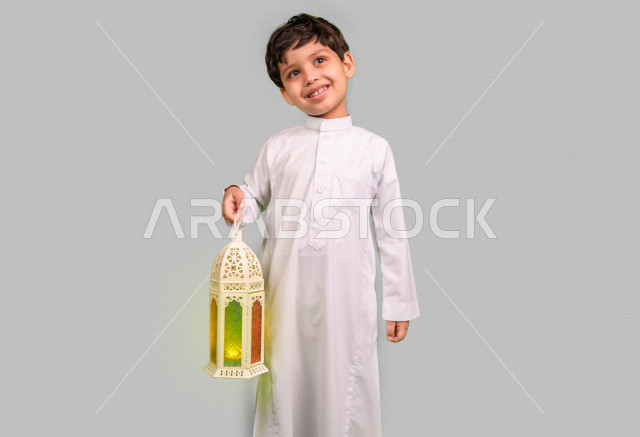 Portrait of a Saudi Arabian Gulf boy holding a lantern while happy, wearing traditional Saudi dress, Ramadan Kareem, white background