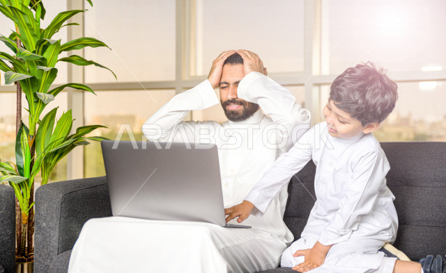 رجل اعمال عربي سعودي خليجي يعمل عن بعد في المنزل لضبط انتشار العدوى ، استخدام الكمبيوتر المحمول لانجاز العمل ، يشعر بالانزعاج بسبب تشويش الابن له اثناء العمل ، اجتماعات اونلاين