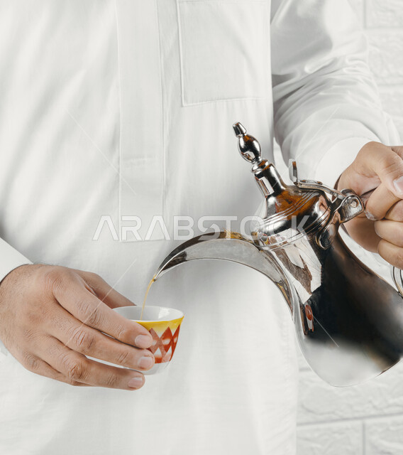 رجل عربي يسكب القهوة العربية الشقراء في فنجان مزخرف باللون الأحمر،  تقديم ضيافة القهوة العربية للضيوف، الزيارة والمناسبات