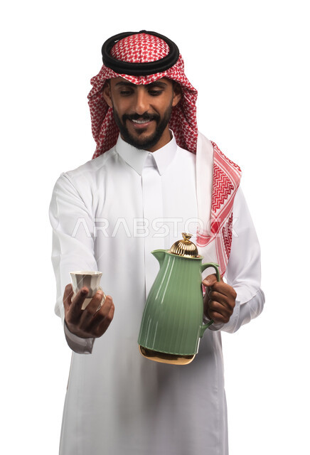 إيماءات وجه تدل على البشاشه والترحيب بالضيوف, أعياد ومناسبات, بورتريه لرجل عربي سعودي خليجي يرتدي الزي السعودي التقليدي يقوم بصب القهوه العربيه, تقديم القهوه الساخنه للضيوف، منتج محلي سعودي ، صنع في السعودية ، منتجات محاصيل سعودية , خلفيه بيضاء