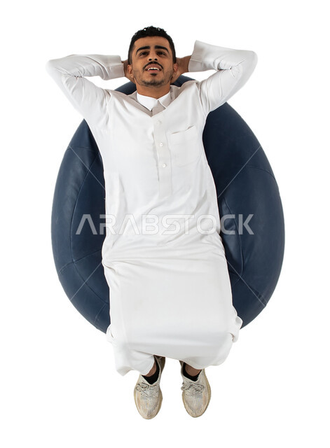 الشعور بالتعب و الخمول , إيماءات يدين تدل على الراحة والإسترخاء ، بورتريه علوي عامودي لرجل عربي سعودي خليجي يرتدي الثوب السعودي يجلس على كرسي طري ومريح ,  الحاجه الى النوم , خلفية بيضاء