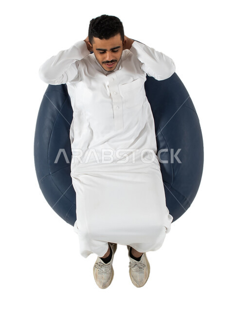 إيماءات يدين تدل على الراحة والإسترخاء ، بورتريه علوي عامودي لرجل عربي سعودي خليجي يرتدي الثوب السعودي يجلس على كرسي طري ومريح , الشعور بالتعب و الخمول , الحاجه الى النوم , خلفية بيضاء