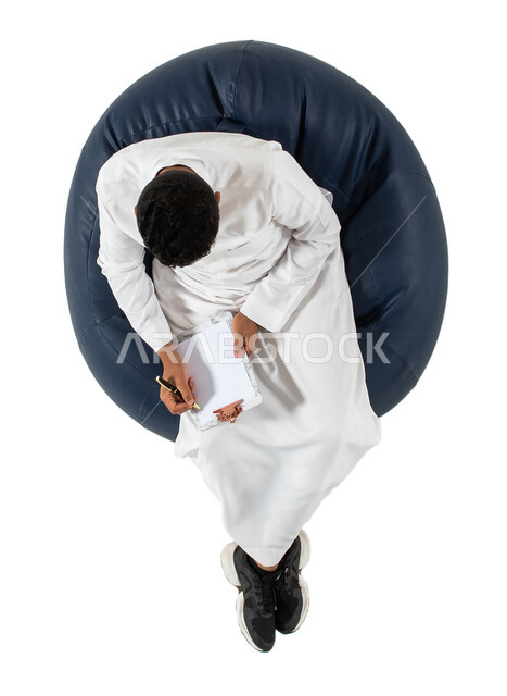 إيماءات وجه ويدين تدل على التفكير و الحيرة ، كتابة وتسجيل الملاحظات ، بورتريه علوي عامودي  لرجل عربي سعودي خليجي يرتدي الزي السعودي يجلس على كرسي مريح ويمسك بيديه ورقة،  التمعن والتركيز ، حل المشكلات واتخاذ القرارات, خلفيه بيضاء