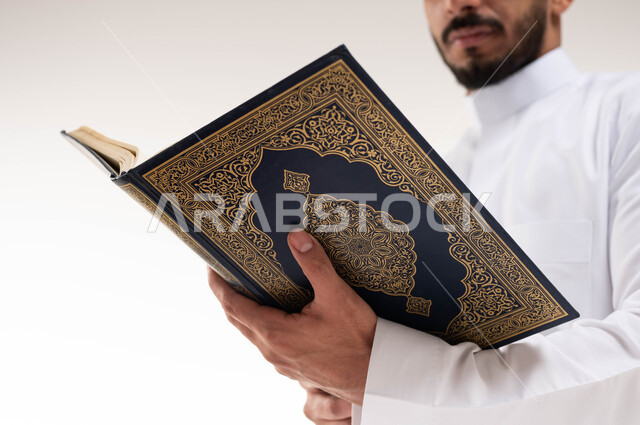 صورة مقربة لرجل عربي خليجي سعودي ، يحمل بيده المصحف الشريف ، قراءة القرآن الكريم ، إسلاميات وعبادة ، تلاوة وحفظ القرآن الكريم ، خلفية بيضاء