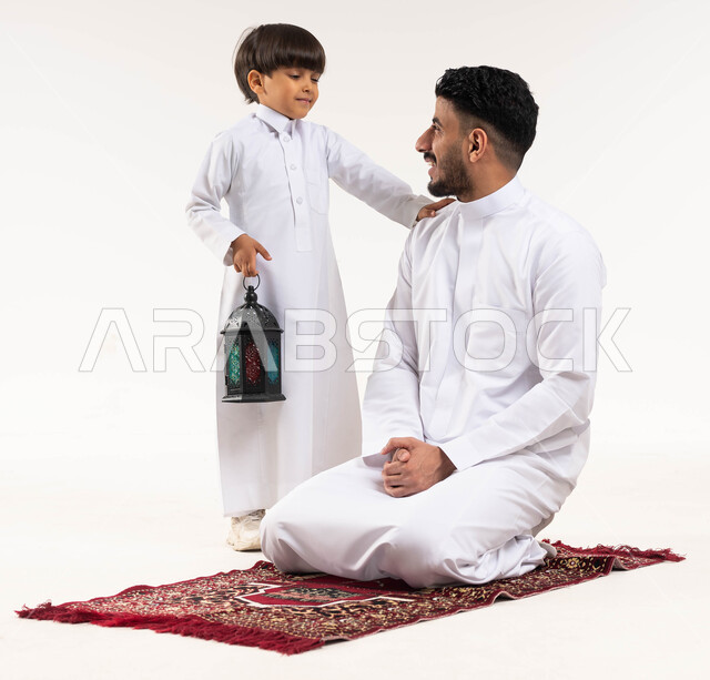 بورتريه لرجل عربي خليجي سعودي مع إبنه ، فانوس رمضان ، الإستعداد لقدوم شهر رمضان المبارك ، المناسبات الدينية والأعياد الإسلامية ، رمضان كريم ، إسلاميات وعبادة ، خلفية بيضاء ، صورة بالطول الكامل