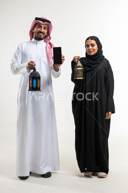 Portrait of a Saudi Arabian Gulf couple, Ramadan lantern, displaying a black screen using a mobile phone, preparing for the advent of the blessed month of Ramadan, religious occasions and Islamic holidays, Ramadan Kareem, Islamic and worship, white backgr