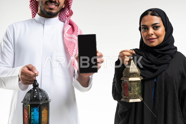 بورتريه لزوجان عربيان خليجيان سعوديان ، فانوس رمضان ، عرض شاشة سوداء بإستخدام الهاتف المحمول ، الإستعداد لقدوم شهر رمضان المبارك ، المناسبات الدينية والأعياد الإسلامية ، رمضان كريم ، إسلاميات وعبادة ، خلفية بيضاء