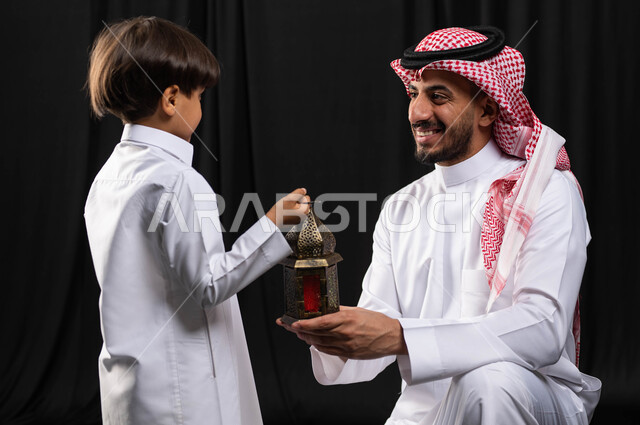 Portrait of a Saudi Arabian Gulf man with his son, Ramadan lantern, preparing for the advent of the blessed month of Ramadan, religious occasions and Islamic holidays, Ramadan Kareem, Islamic and worship, black background