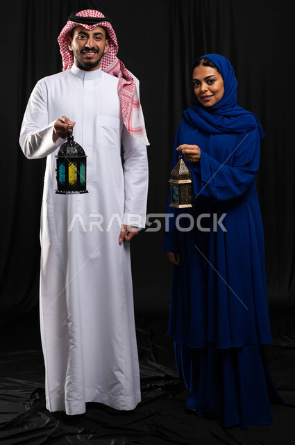 بورتريه لزوجان عربيان خليجيان سعوديان ، فانوس رمضان ، الإستعداد لقدوم شهر رمضان المبارك ، المناسبات الدينية والأعياد الإسلامية ، رمضان كريم ، إسلاميات وعبادة ، خلفية سوداء ، صورة بالطول الكامل