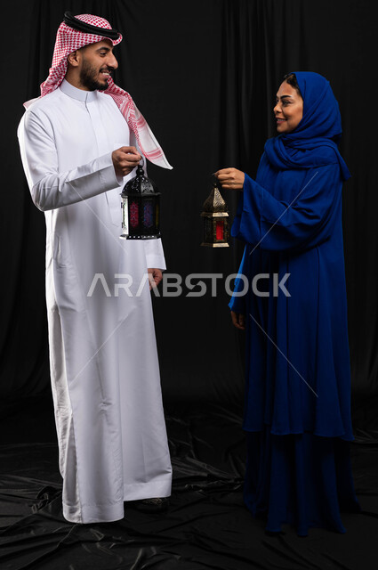 بورتريه لزوجان عربيان خليجيان سعوديان ، فانوس رمضان ، الإستعداد لقدوم شهر رمضان المبارك ، المناسبات الدينية والأعياد الإسلامية ، رمضان كريم ، إسلاميات وعبادة ، خلفية سوداء ، صورة بالطول الكامل
