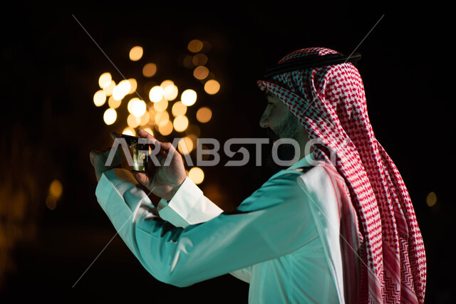 صورة من الخلف لرجل عربي خليجي سعودي يستخدم الهاتف المحمول المحمول، استخدام وسائل التواصل الاجتماعي، التقاط الصور من خلال الهاتف المحمول، كاميرا خلفية، بث مباشر، حدائق ومنتزهات