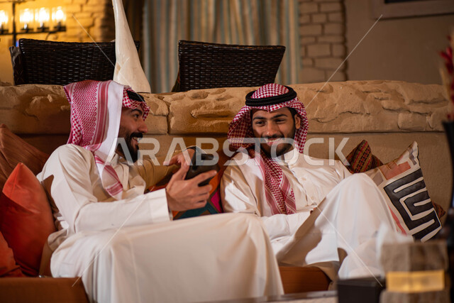 رجلان عربيان خليجيان سعوديان يرتديان الزي السعودي ويقضيان اوقات ممتعة، استخدام الهاتف المحمول، صداقات شباب، نقاشات وحوارات، تقنيات حديثة، جلسة شبابية
