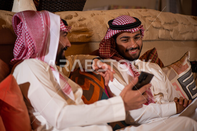 رجلان عربيان خليجيان سعوديان يرتديان الزي السعودي ويقضيان اوقات ممتعة، استخدام الهاتف المحمول، صداقات شباب، نقاشات وحوارات، تقنيات حديثة، جلسة شبابية