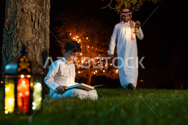 رجل عربي خليجي سعودي وابنه، قراءة القرآن الكريم، المصحف الشريف، تلاوة وتحفيظ القرآن الكريم للأطفال، فانوس رمضان، استقبال شهر رمضان المبارك، زينة شهر رمضان، أجواء رمضانية، جلسة خارجية في الهواء الطلق