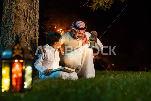 رجل عربي خليجي سعودي وابنه، قراءة القرآن الكريم، المصحف الشريف، تلاوة وتحفيظ القرآن الكريم للأطفال، فانوس رمضان، استقبال شهر رمضان المبارك، زينة شهر رمضان، أجواء رمضانية، جلسة خارجية في الهواء الطلق