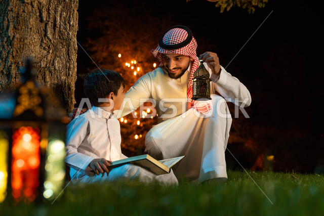 رجل عربي خليجي سعودي وابنه، قراءة القرآن الكريم، المصحف الشريف، تلاوة وتحفيظ القرآن الكريم للأطفال، فانوس رمضان، استقبال شهر رمضان المبارك، زينة شهر رمضان، أجواء رمضانية، جلسة خارجية في الهواء الطلق