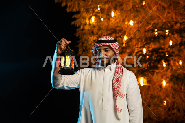 رجل عربي خليجي سعودي يحمل بيده فانوس مضيء، استقبال شهر رمضان المبارك، المناسبات الدينية والأعياد الإسلامية، فانوس رمضان، زينة شهر رمضان، أجواء رمضانية