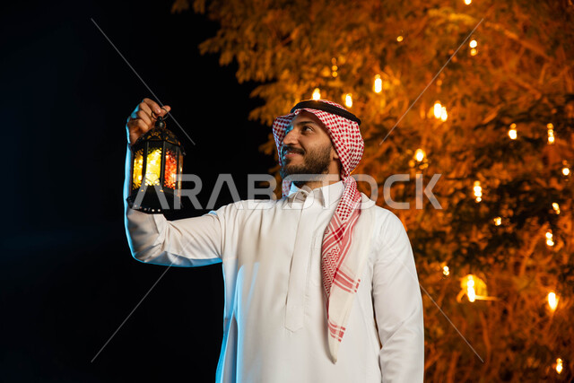 رجل عربي خليجي سعودي يحمل بيده فانوس مضيء، استقبال شهر رمضان المبارك، المناسبات الدينية والأعياد الإسلامية، فانوس رمضان، زينة شهر رمضان، أجواء رمضانية