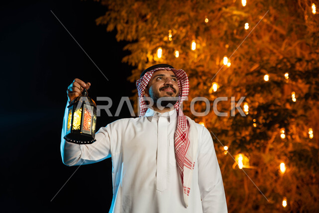 رجل عربي خليجي سعودي يحمل بيده فانوس مضيء، استقبال شهر رمضان المبارك، المناسبات الدينية والأعياد الإسلامية، فانوس رمضان، زينة شهر رمضان، أجواء رمضانية