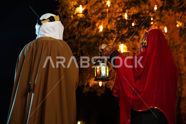 زوجان عربيان سعوديان خليجيان يرتديان زي تراثي شعبي سعودي، استقبال شهر رمضان المبارك، فانوس رمضان، زينة شهر رمضان، أجواء رمضانية، زي شعبي سعودي، يوم التأسيس السعودي