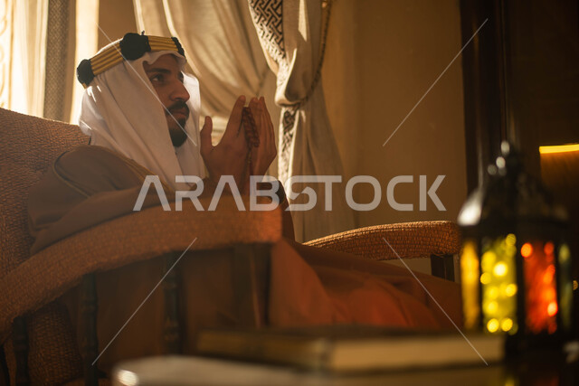 رجل عربي خليجي سعودي يرتدي زي تراثي سعودي للمناسبات الوطنية ويرفع يديه لأعلى، الدعاء، ذكر الله، إستقبال شهر رمضان المبارك، فانوس رمضان، أجواء رمضانية، يوم التأسيس السعودي
