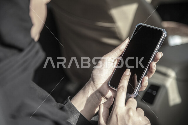 سيدة عربية خليجية سعودية داخل السيارة تحمل بيدها الهاتف المحمول ،استخدام تطبيق خدمة توصيل الركاب ، تحديد الموقع ،  عرض خاصية التتبع ، التاكسي الاخضر في السعودية