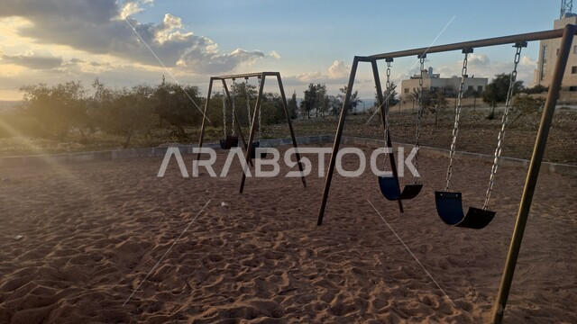 ارجوحة معدنية فارغة في احد الحدائق العامة، الاشجار والنباتات الخضراء، ارجوحة اطفال، مقعد الارجوحة معلق بالسلاسل الحديدية، حدائق ومنتزهات عامة، منطقة مخصصة لالعاب الاطفال