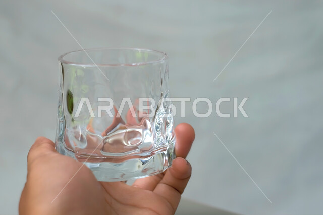 يد رجل يمسك كوب زجاجي فارغ  , كأس كريستال على خلفية بيضاء , كوب ماء شفاف , عرض المنتجات . 