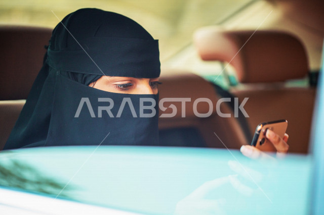 سيدة عربية خليجية سعودية داخل السيارة تحمل بيدها الهاتف المحمول ،استخدام تطبيق خدمة توصيل الركاب ، تحديد الموقع ،  عرض خاصية التتبع ، التاكسي الاخضر في السعودية