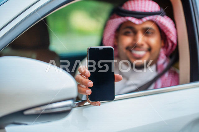 رجل عربي خليجي سعودي مبتسم داخل السيارة يحمل بيده الهاتف المحمول ،عرض تطبيق خدمة توصيل الركاب ، تحديد الموقع ،  عرض خاصية التتبع ، التاكسي الاخضر في السعودية