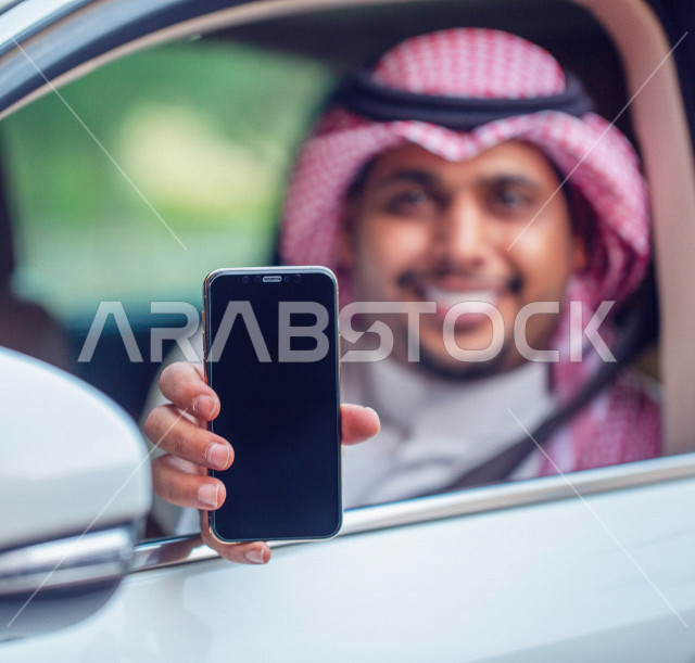 رجل عربي خليجي سعودي مبتسم داخل السيارة يحمل بيده الهاتف المحمول ،عرض تطبيق خدمة توصيل الركاب ، تحديد الموقع ،  عرض خاصية التتبع ، التاكسي الاخضر في السعودية