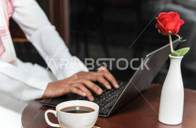 A Saudi Arabian Gulf businessman sitting in a coffee shop, working meeting outside the company, completing work tasks via a computer, managing business remotely, enjoying drinking coffee in a coffee shop, cafes in the Kingdom of Saudi Arabia