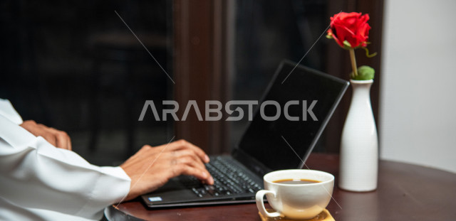 A Saudi Arabian Gulf businessman sitting in a coffee shop, working meeting outside the company, completing work tasks via a computer, managing business remotely, enjoying drinking coffee in a coffee shop, cafes in the Kingdom of Saudi Arabia