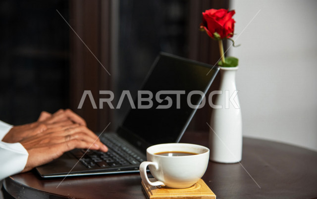 رجل أعمال عربي سعودي خليجي يجلس في المقهى, إجتماع عمل في خارج الشركه, انجهاز مهام العمل عبر جهاز الحاسوب, إدارة الأعمال عن بعد, الإستمتاع بشرب القهوه في متجر القهوه, مقاهي في المملكه العربيه السعوديه