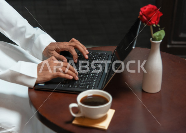 رجل أعمال عربي سعودي خليجي يجلس في المقهى, إجتماع عمل في خارج الشركه, انجهاز مهام العمل عبر جهاز الحاسوب, إدارة الأعمال عن بعد, الإستمتاع بشرب القهوه في متجر القهوه, مقاهي في المملكه العربيه السعوديه