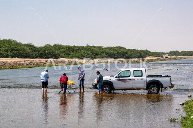 Young Saudi Gulf Arabs standing in the middle of the Jeddah River in the Green Valley in the Kingdom of Saudi Arabia, white car, green trees and plants, water stream, landscapes, nature background