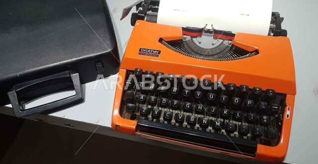 صوة مقربة لالة كتابة، الآلة الطابعة القديمة، الة كتابة برتقالية اللون، آلة كاتبة كلاسيكية قديمة