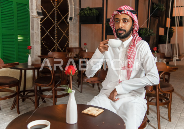 رجل عربي سعودي خليجي يجلس في مقهى, طلب القهوه من متجر القهوه السعودي, الإستمتاع بشرب القهوه في أجواء هادئه, قضاء وقت ممتع خارج المنزل, تسليه وترفيه، مقاهي في المملكه العربيه السعوديه