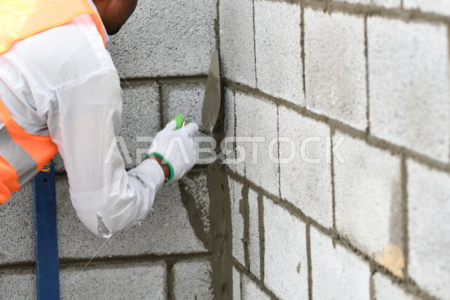 صورة مقربة لعامل بناء يقوم ببناء جدار من الطوب والاسمنت، قالب طوبي، اعمال البناء، حائط حجري، ادوات ومعدات البناء