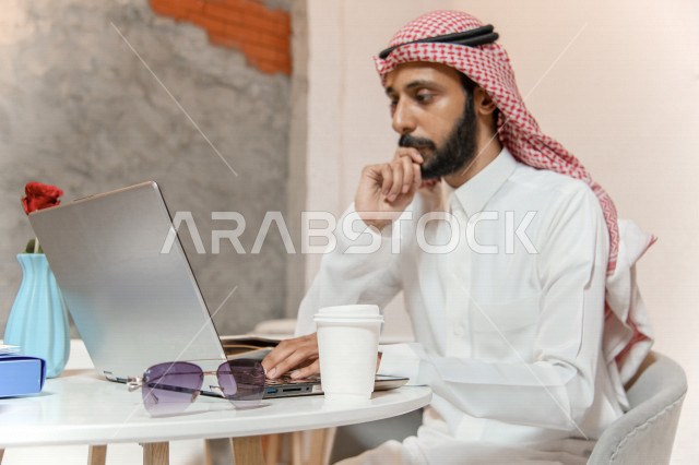 رجل أعمال عربي سعودي خليجي في المقهى, إجتماع عمل عن بعد, انجهاز مهام العمل عبر جهاز الحاسوب, إدارة الأعمال خارج الشركه,  الإستمتاع بشرب القهوه في متجر القهوه, مقاهي في المملكه العربيه السعوديه