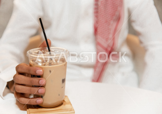 رجل عربي سعودي خليجي يجلس في مقهى, طلب القهوه من متجر القهوه السعودي, الإستمتاع بشرب القهوه البارده في أجواء هادئه, قضاء وقت ممتع خارج المنزل, تسليه وترفيه، مقاهي في المملكه العربيه السعوديه