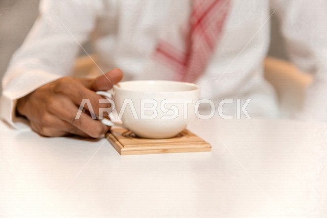 رجل عربي سعودي خليجي يجلس في مقهى, طلب القهوه من متجر القهوه السعودي, الإستمتاع بشرب القهوه في أجواء هادئه, قضاء وقت ممتع خارج المنزل, تسليه وترفيه، مقاهي في المملكه العربيه السعوديه