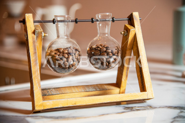 حبوب البن الطازجه في زجاجات جميله على طاوله في المقهى, صنع القهوه من حبوب القهوه المحمصه الشهيه, كافيين, تزيين المقهى بزجاجات مليئه بحبوب القهوه المحمصه السوداء, تحميص وطحن البن الطازج, متجر القهوه السعودي